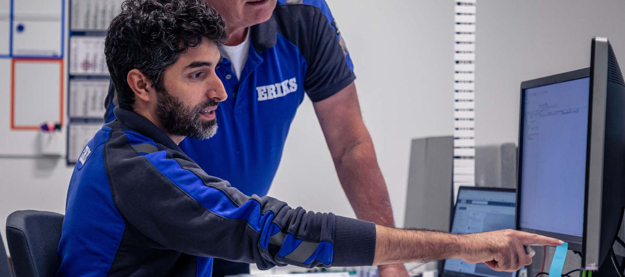 Zwei ERIKS Mitarbeiter arbeiten gemeinsam an einem Computer, wobei einer auf den Bildschirm zeigt und der andere zusieht.