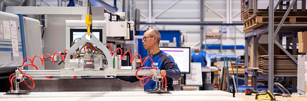 Ein ERIKS Mitarbeiter bedient eine Maschine mit Saugnäpfen, um große Kunststoffplatten anzuheben und in einem gut organisierten industriellen Arbeitsbereich zu transportieren.