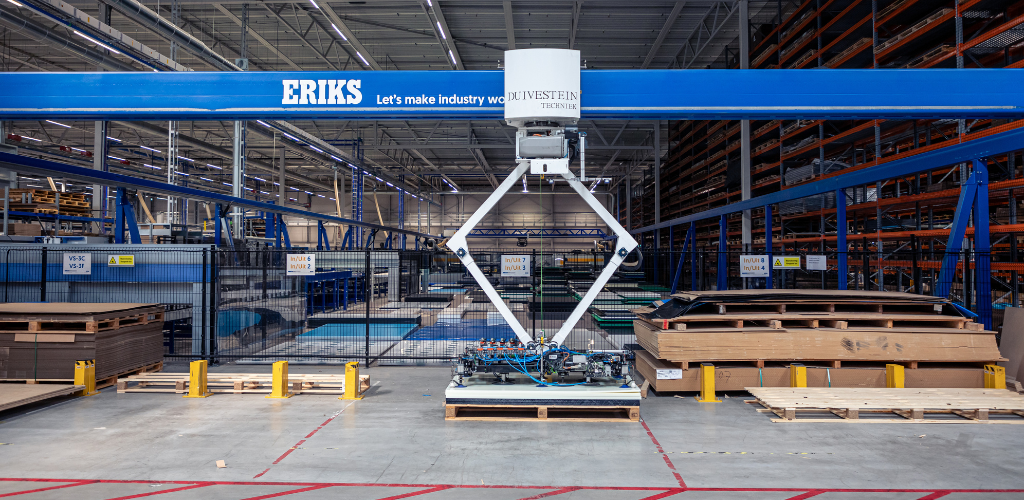 Een grote ERIKS-bovenloopkraan in een ruime opslagplaats, uitgerust met een robotisch heftmechanisme, omringd door netjes gestapelde pallets en stellingen.