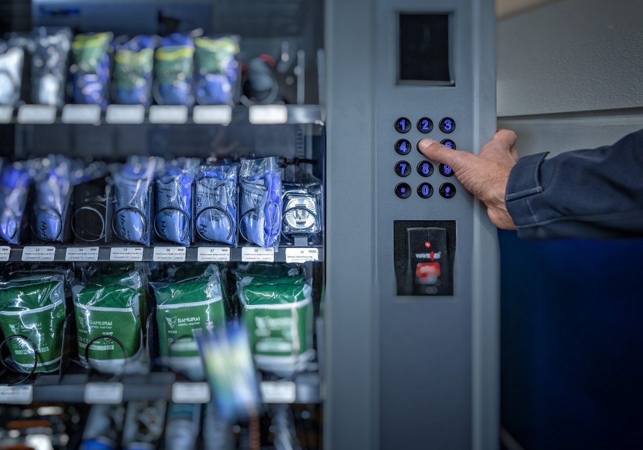Mitarbeiter drückt am Ausgabeautomaten auf eine Zahl, um das Material zu erhalten.