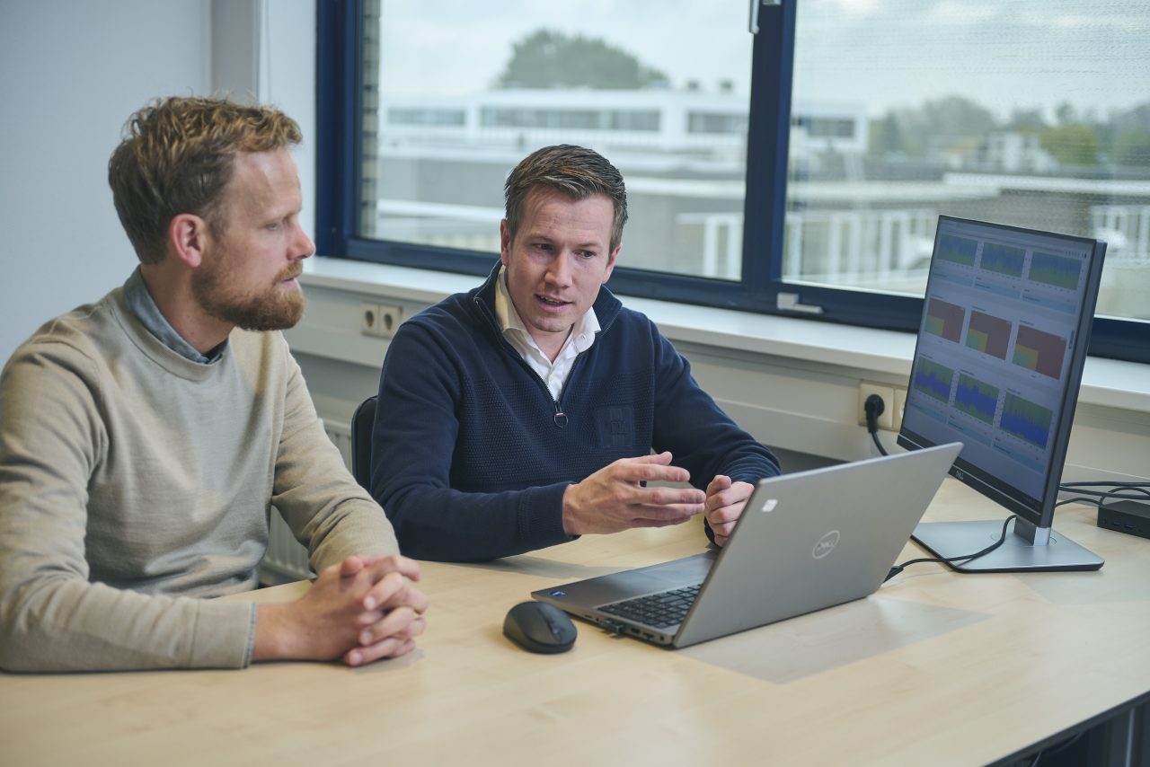  Zwei Männer diskutieren etwas vor einem Laptop mit Diagrammen auf dem Bildschirm