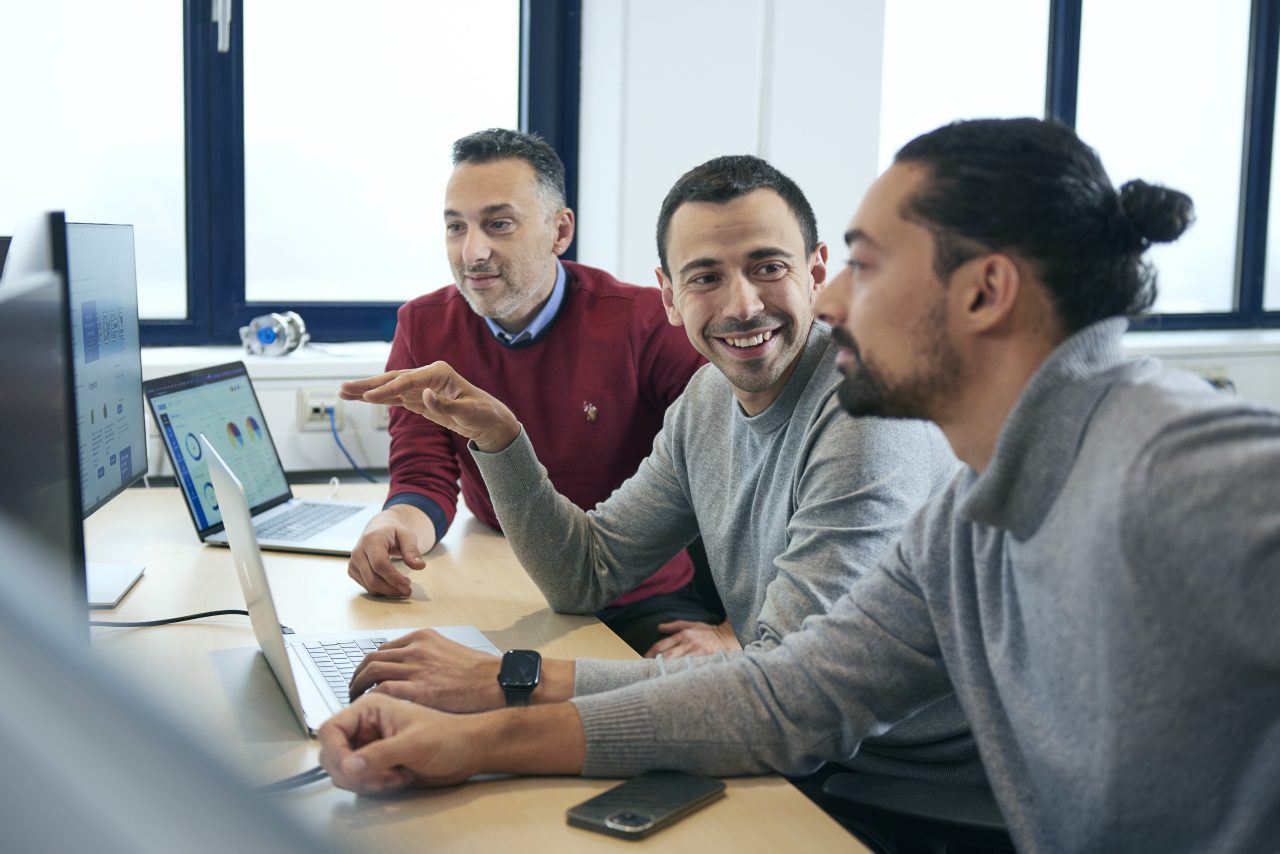 Drei Kollegen lächeln und arbeiten gemeinsam an einem Laptop