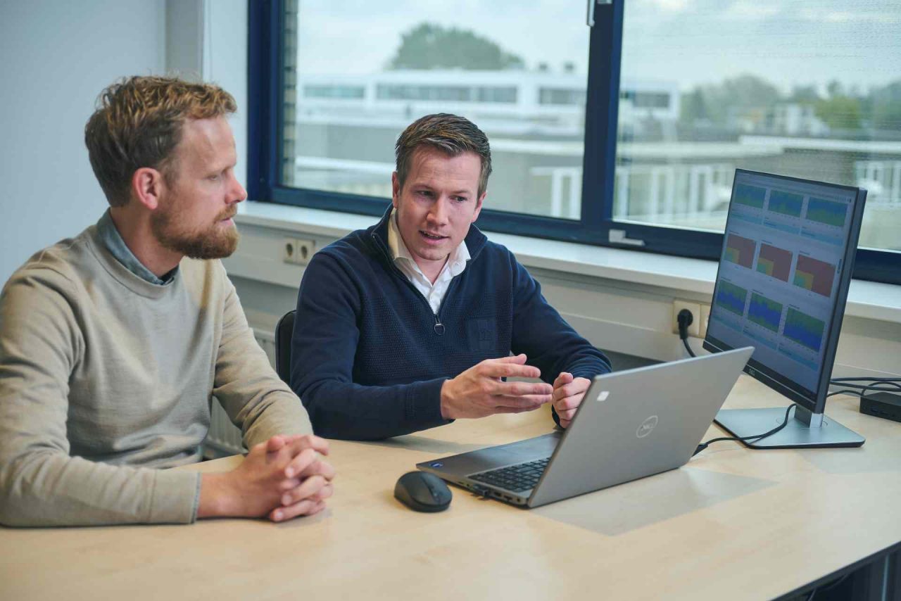 Zwei Männer diskutieren etwas vor einem Laptop mit Diagrammen auf dem Bildschirm