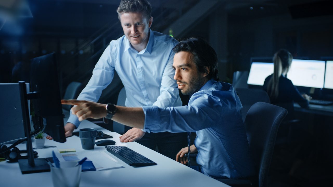 Strategic Account Manager Zwei Männer arbeiten gemeinsam an einem Computerbildschirm.