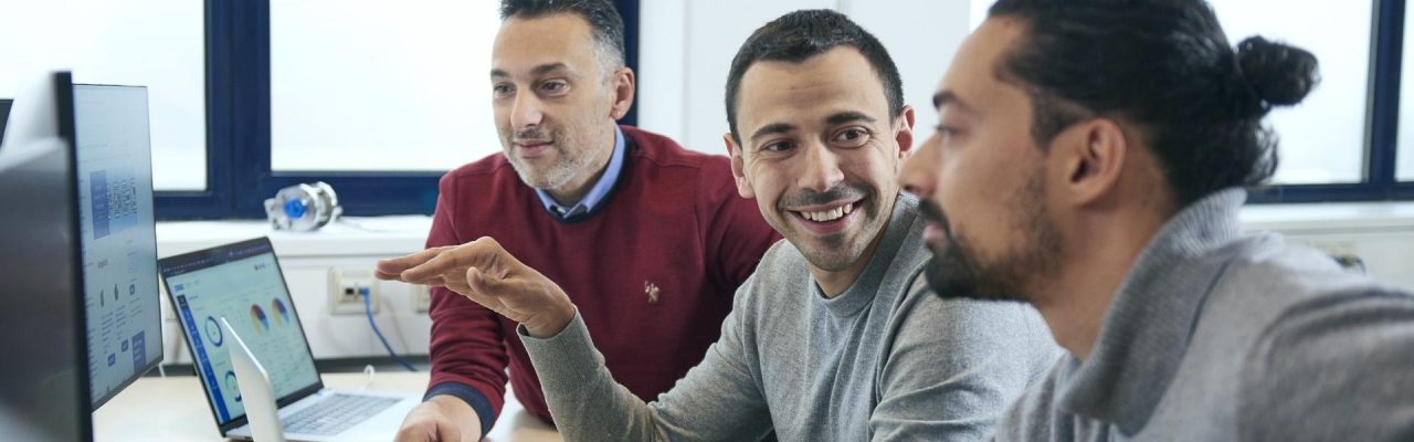 Drei Kollegen lächeln und arbeiten gemeinsam an einem Laptop